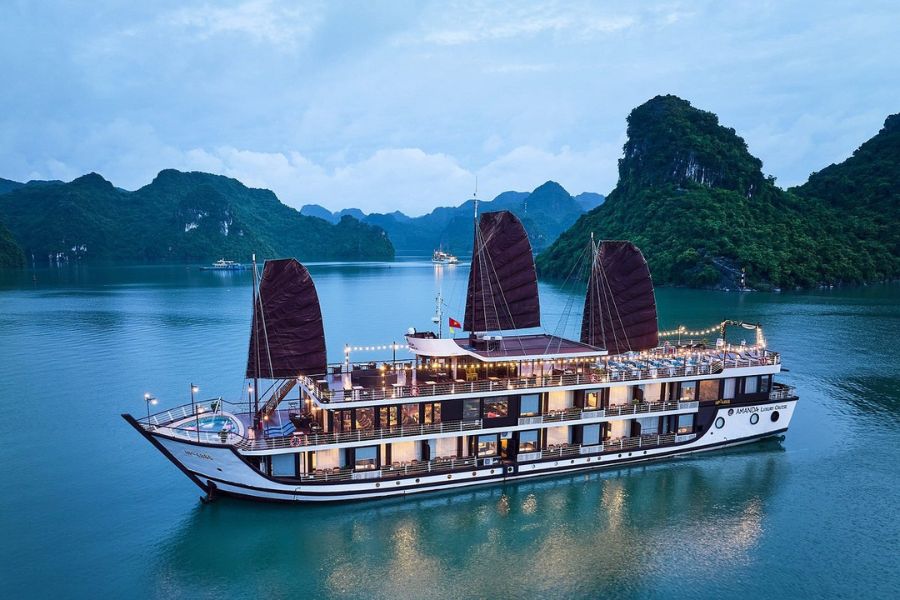 Amanda Halong junk boat with red sails and string lights at golden hour on the bay
