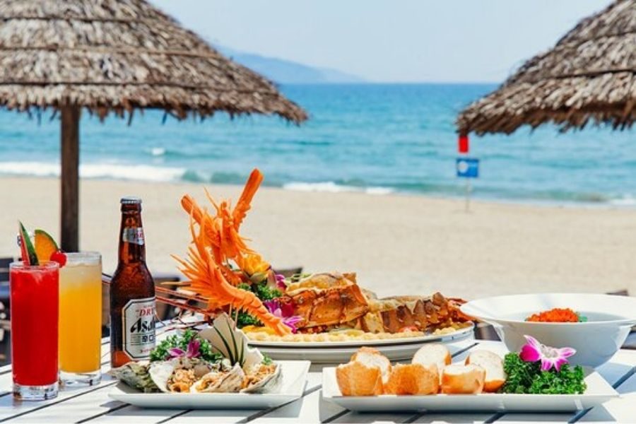 Beachfront seafood dining with grilled lobster, prawns, colorful drinks, and thatched umbrellas at Muoi Bien Da Nang