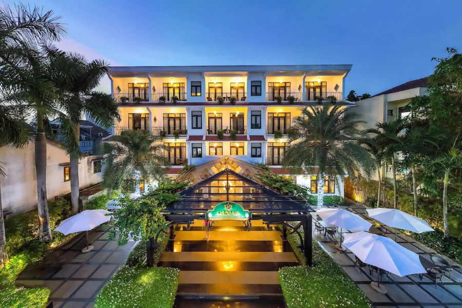 Colonial-style hotel lit up at dusk with courtyard pool, palm trees, and white umbrellas