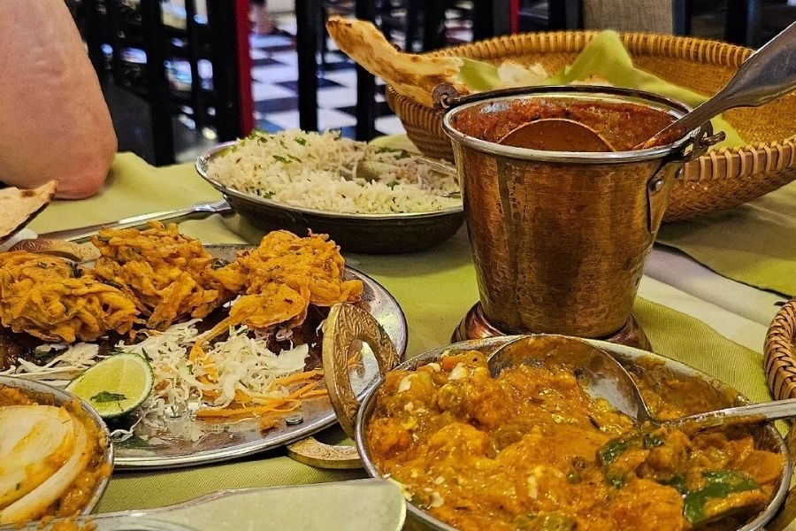 Indian vegetarian feast with paneer curry, jeera rice, pakoras, dal, naan bread in copper bucket on green tablecloth