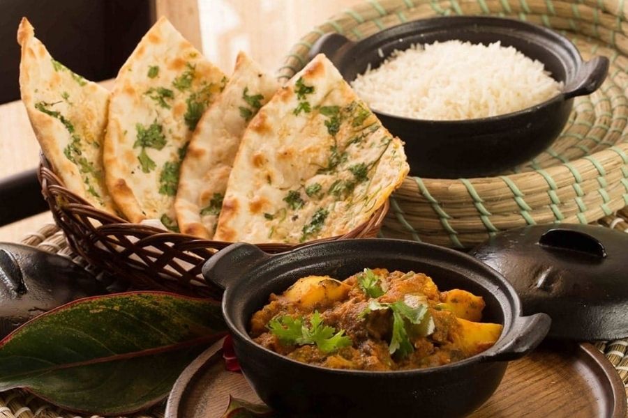 Indian vegetarian meal with garlic naan bread, potato curry in cast iron pot