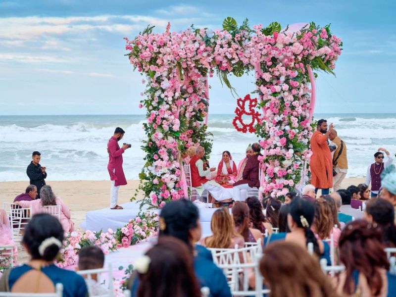 Minimalist white floral wedding altar on a sandy beach with the blue ocean in the background.