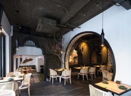 Modern dining space with black arched doorways, white rattan chairs, exposed ceiling, and tree decor