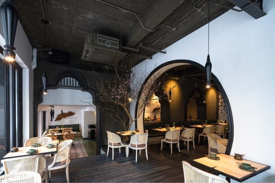 Modern dining space with black arched doorways, white rattan chairs, exposed ceiling, and tree decor