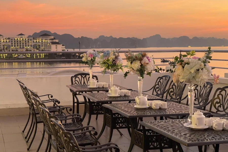 Rooftop terrace with sunset view of Ha Long Bay, outdoor dining tables, and wrought iron chairs