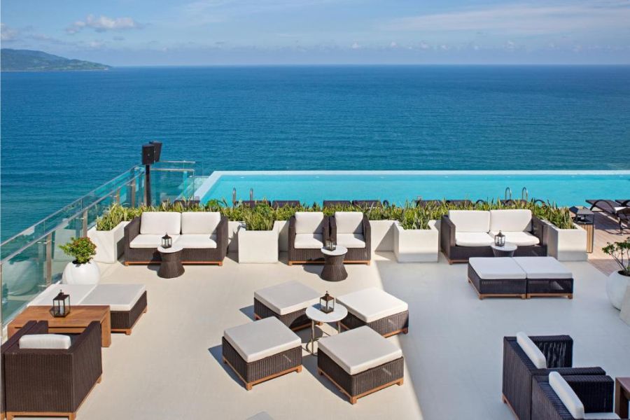 Luxurious rooftop deck with white wicker loungers, infinity pool, and endless ocean horizon