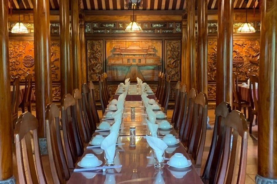 Long banquet table inside a Vietnamese wooden house with carved wall art