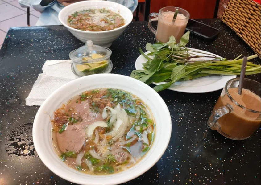 Two bowls of halal beef pho with fresh herbs and iced coffee