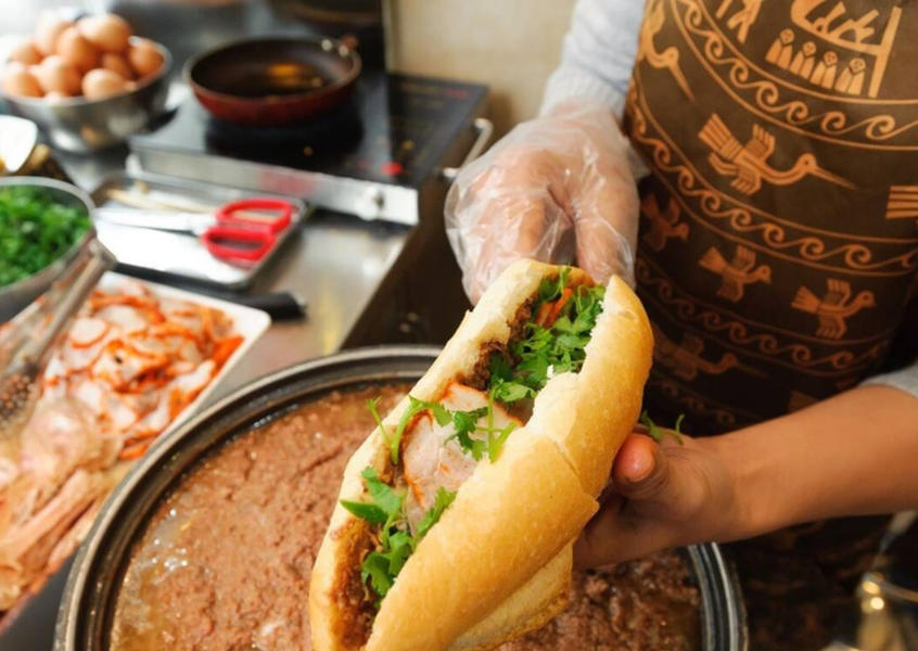 A hand holding a freshly made Vietnamese banh mi sandwich