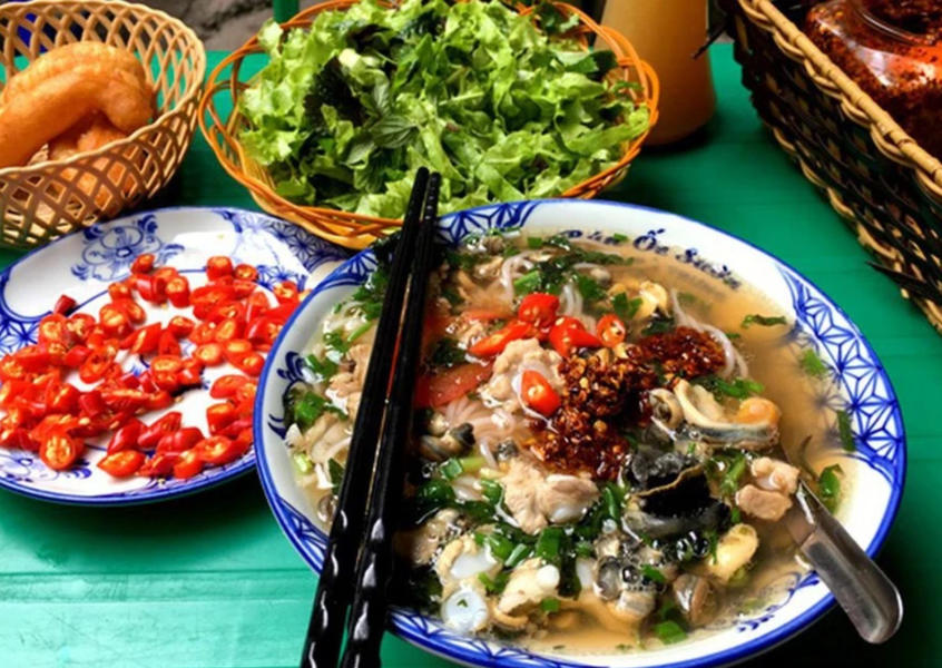 A bowl of Vietnamese snail noodle soup with herbs and chili