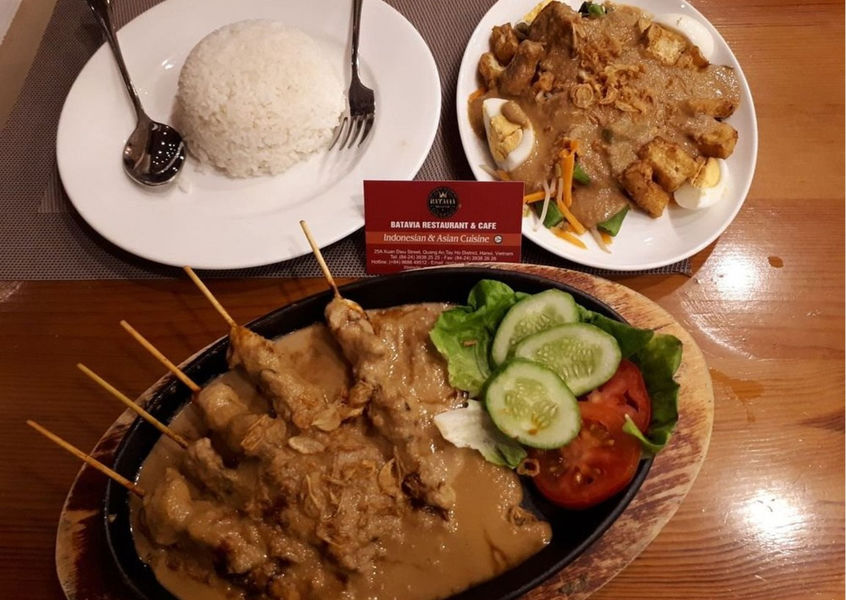 Plates of rice, chicken satay with sauce, and gado-gado