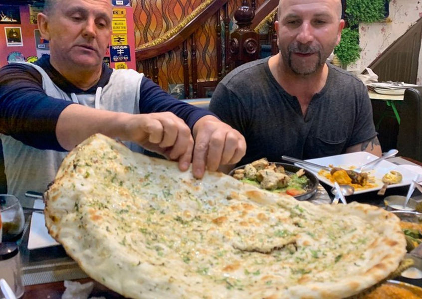 Two men eating a large piece of naan bread at a table