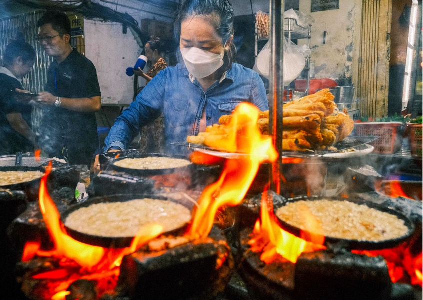 Street food vendor cooking banh xeo crepes over open flame