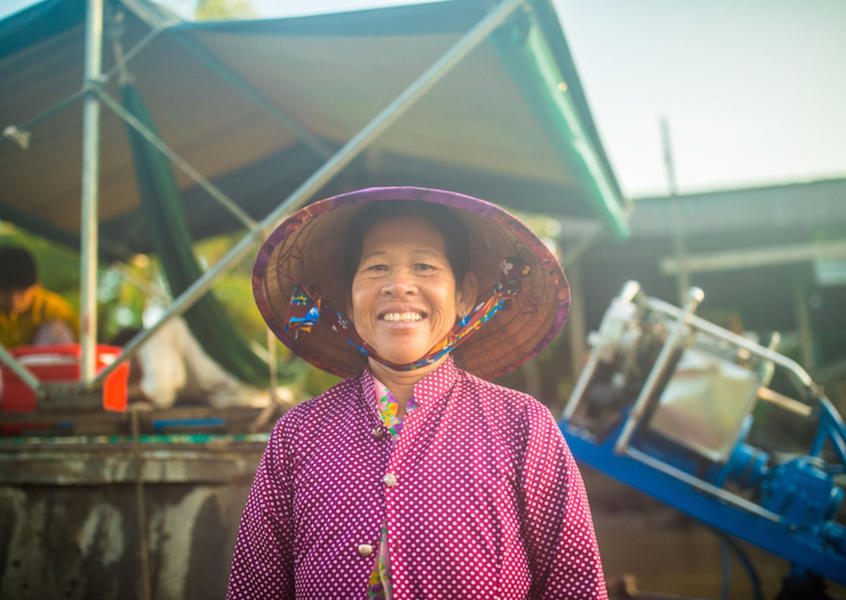 A smiling Vietnamese woman wearing a traditional nón lá conical hat at a floating market in the Mekong Delta