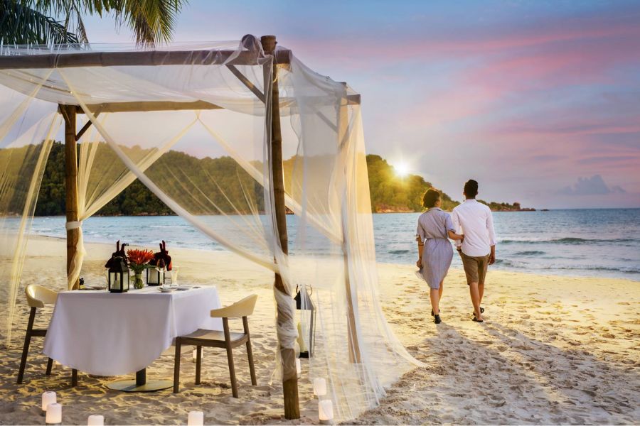 Couple walking beach at sunset near private dinner cabana