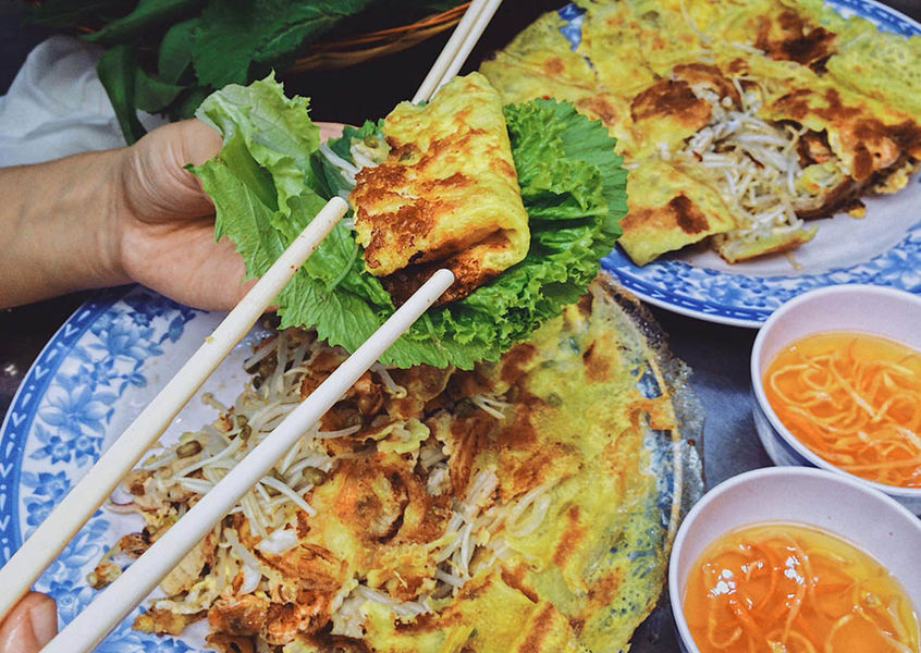 Hand holding crispy bánh xèo pancake wrapped in lettuce