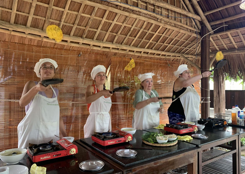 Travelers flipping banh xeo pancake in cooking class