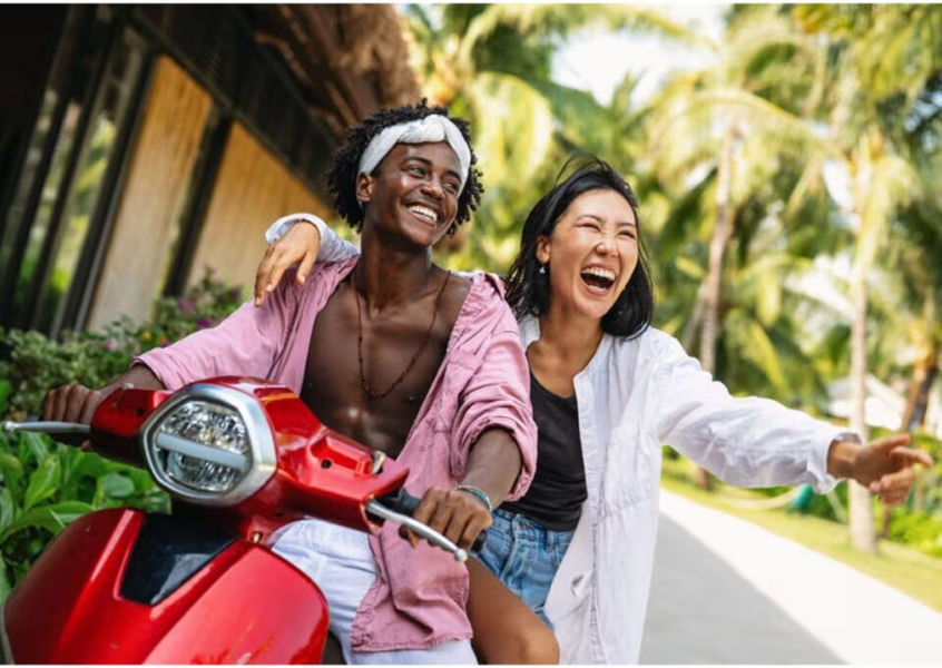 Couple riding a red scooter at a tropical resort