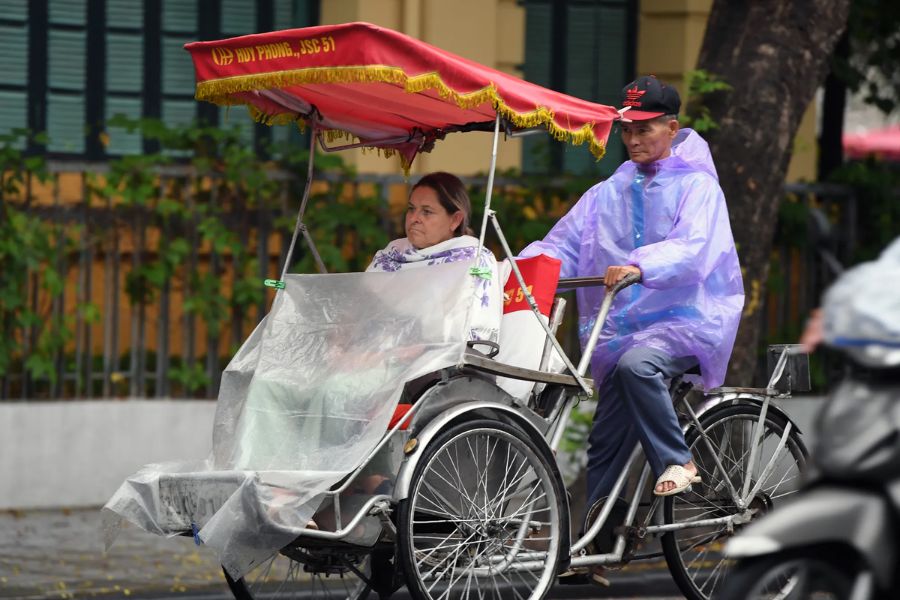Tourists ride a cyclo in rain ponchos on a rainy Hanoi street