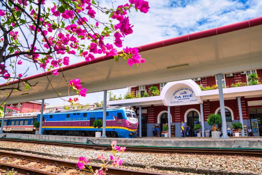 Reunification Express train arriving at Hue train station in Vietnam, framed by blooming bougainvillea