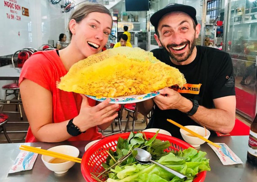 Tourists holding a giant crispy bánh xèo pancake, Saigon eatery