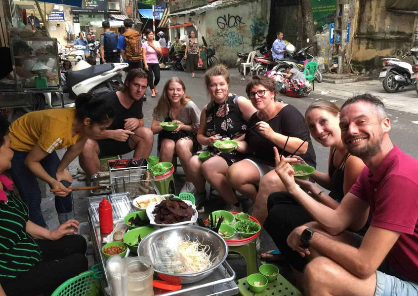 Tourists enjoying street food with a local vendor in Hanoi