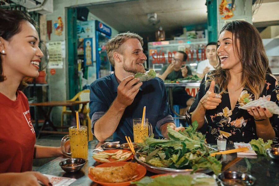 Travelers enjoying fresh Vietnamese spring rolls and local drinks at a street side eatery