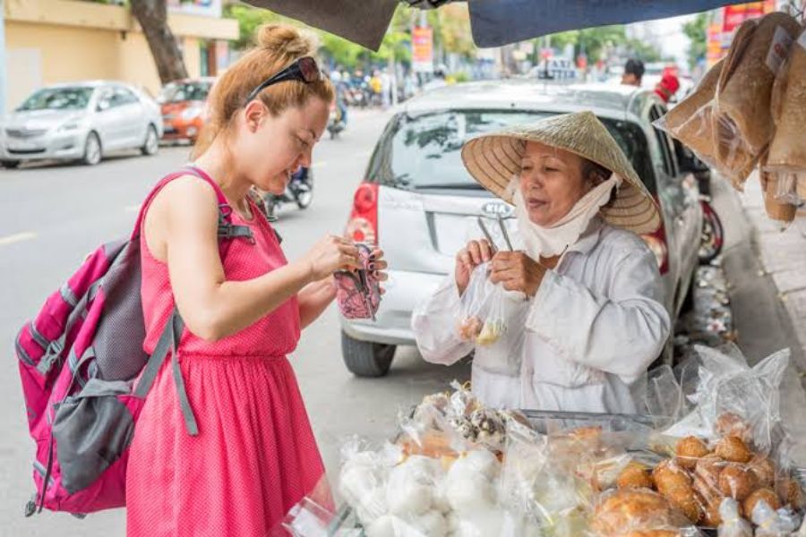 Tourist buying street food from a Vietnamese vendor wearing a conical hat