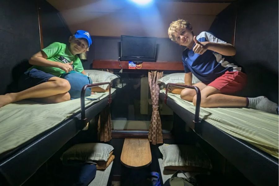 Two young travelers on bunk beds inside a soft berth cabin on a Vietnam sleeper train at night