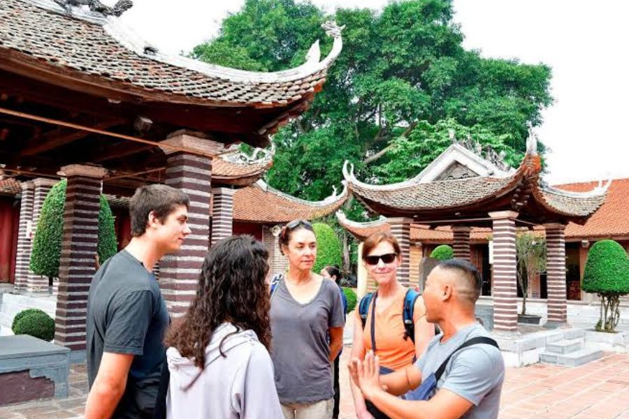Tour guide explaining temple etiquette to a group of travelers in a Vietnamese pagoda courtyard
