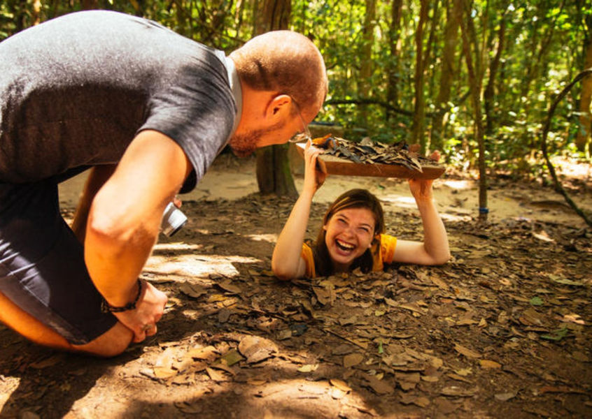 Tourist laughing while climbing out of a narrow underground tunnel opening at the Cu Chi Tunnels near Ho Chi Minh City