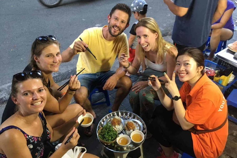 Group tasting street food on plastic stools with a local guide