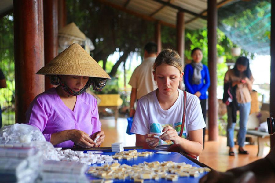 Local artisan guiding a traveler through hand-wrapping coconut candy at a Mekong Delta workshop