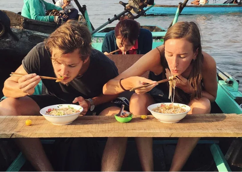 Couple eating noodle soup from boat-side vendors while cruising the Mekong Delta floating market