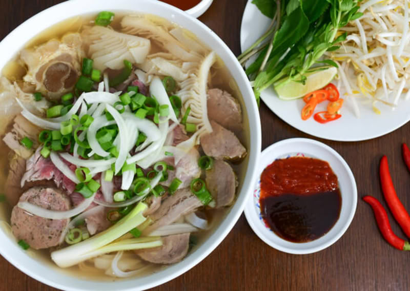 Bowl of pho with beef, herbs, and chili sauce