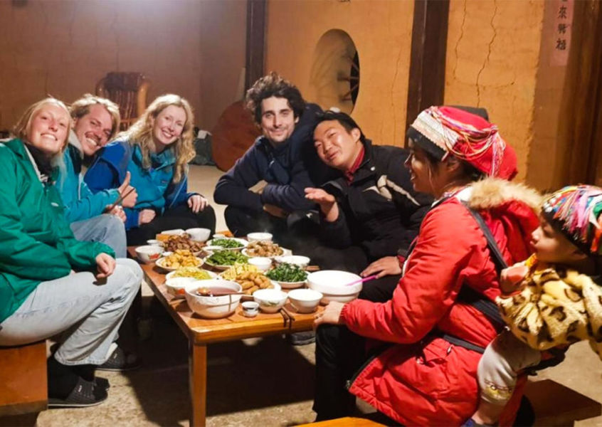 Travelers sharing a traditional dinner with an ethnic minority host family during a homestay in the northern Vietnam highlands