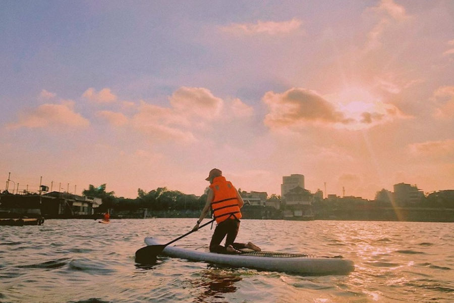 Paddleboarder in a life jacket on calm water at sunset