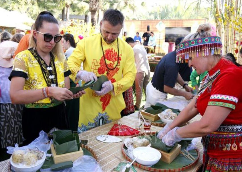 Travelers in traditional costumes wrapping banh chung sticky rice cakes during a Tet Lunar New Year cultural activity
