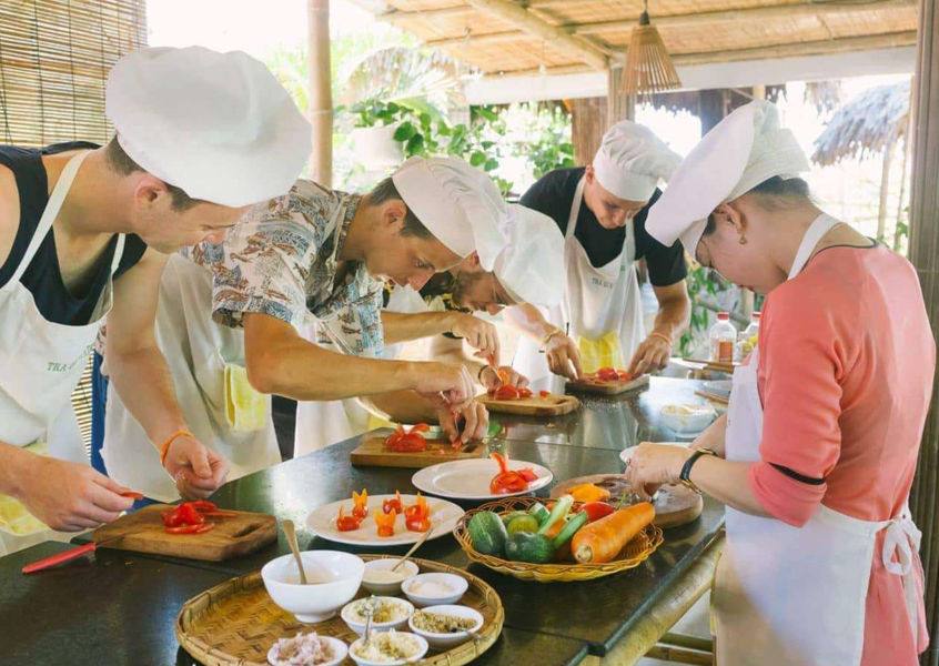 Group of travelers in chef hats plating fresh vegetables during a hands-on Vietnamese cooking class