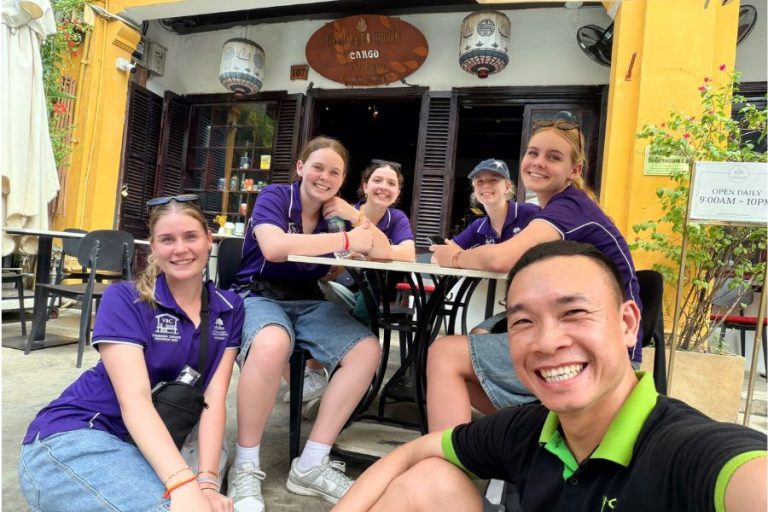 Smiling local Vietnamese guide with a group of international travellers at a street café